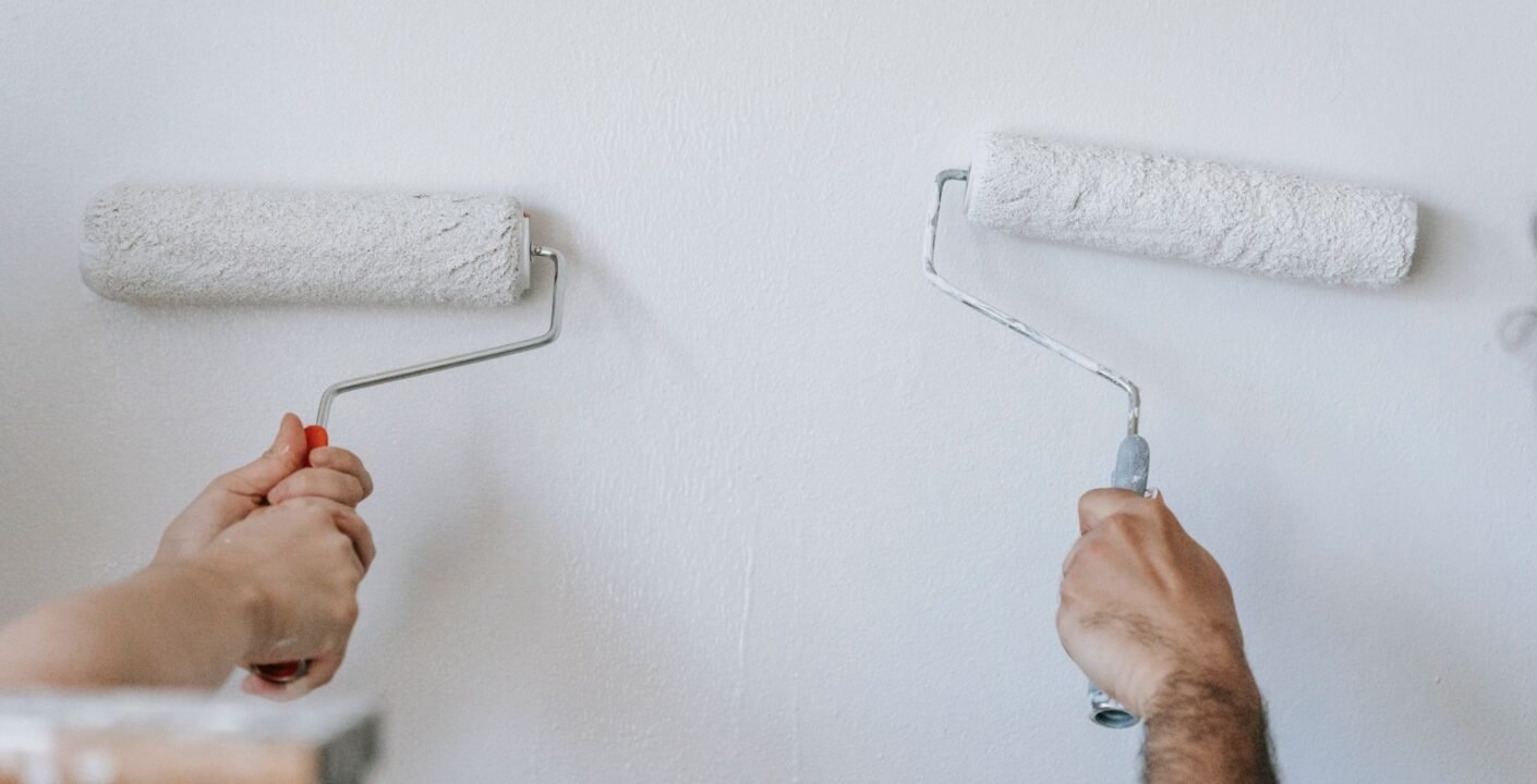 Zwei Personen streichen eine Wand mit Farbrollen bei Renovierungsarbeiten