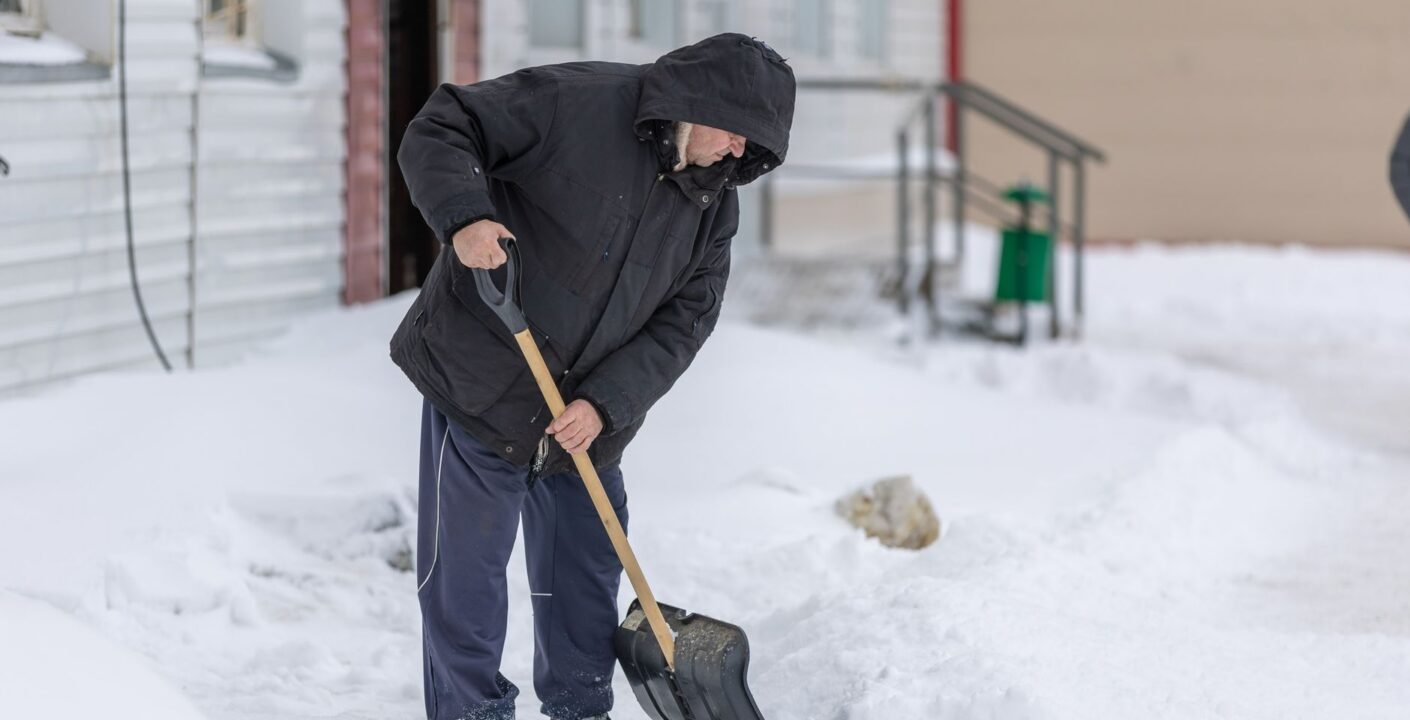 Räumen eines Gehwegs mit der Schneeschaufel vor einem Gebäude